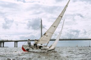 pexels photo 4934616 4934616 A sailboat with two people navigating the ocean beneath a large bridge on a cloudy day.